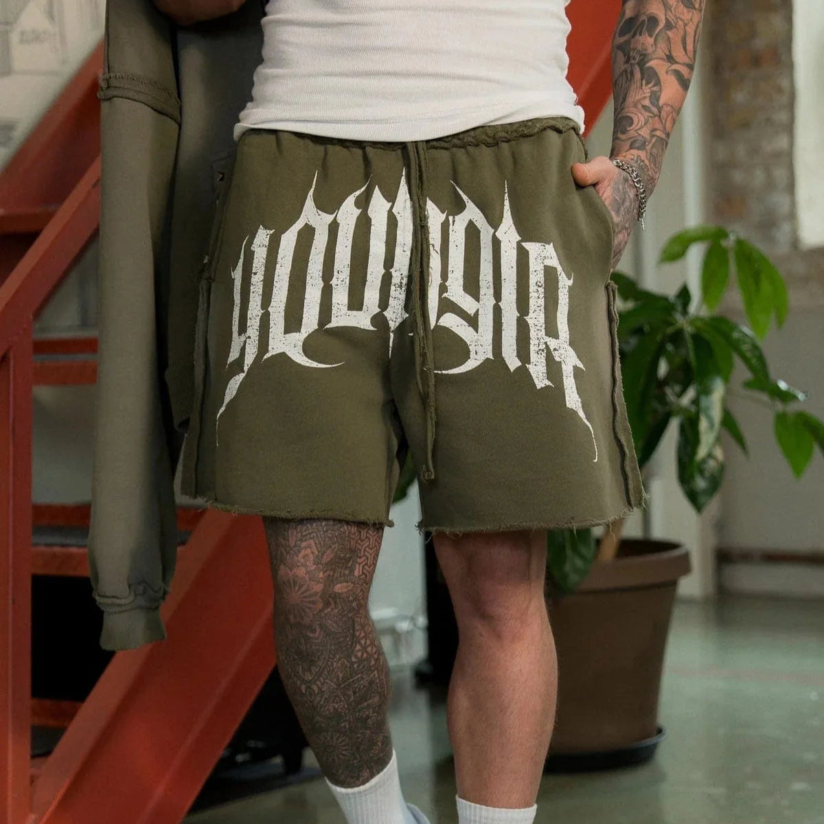 Person wearing green shorts with 'Yonger' printed on them, standing indoors.