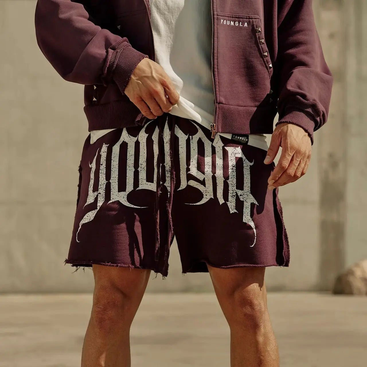 Person wearing a maroon jacket, white sneakers, and shorts with text on a concrete surface.